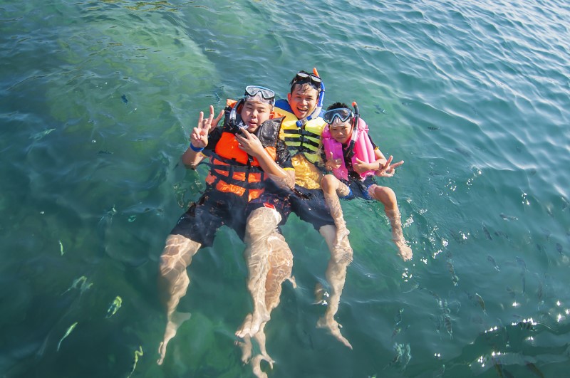 Tiga laki-laki berenang terapung di laut dengan bahagia.