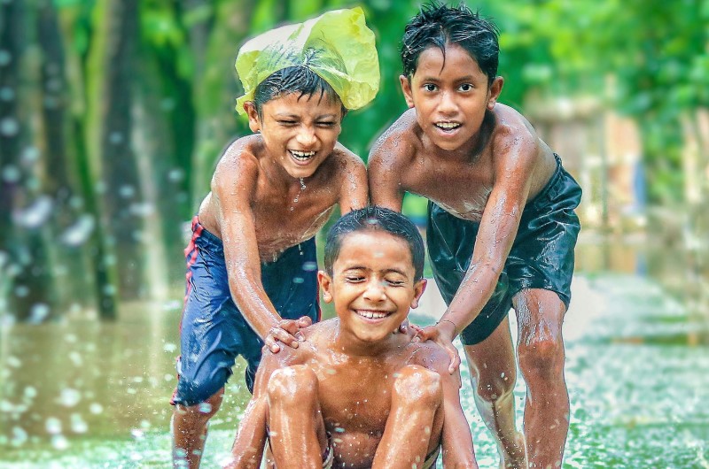 Tiga orang anak laki-laki sedang bermain seluncuran kayu di genangan air hujan